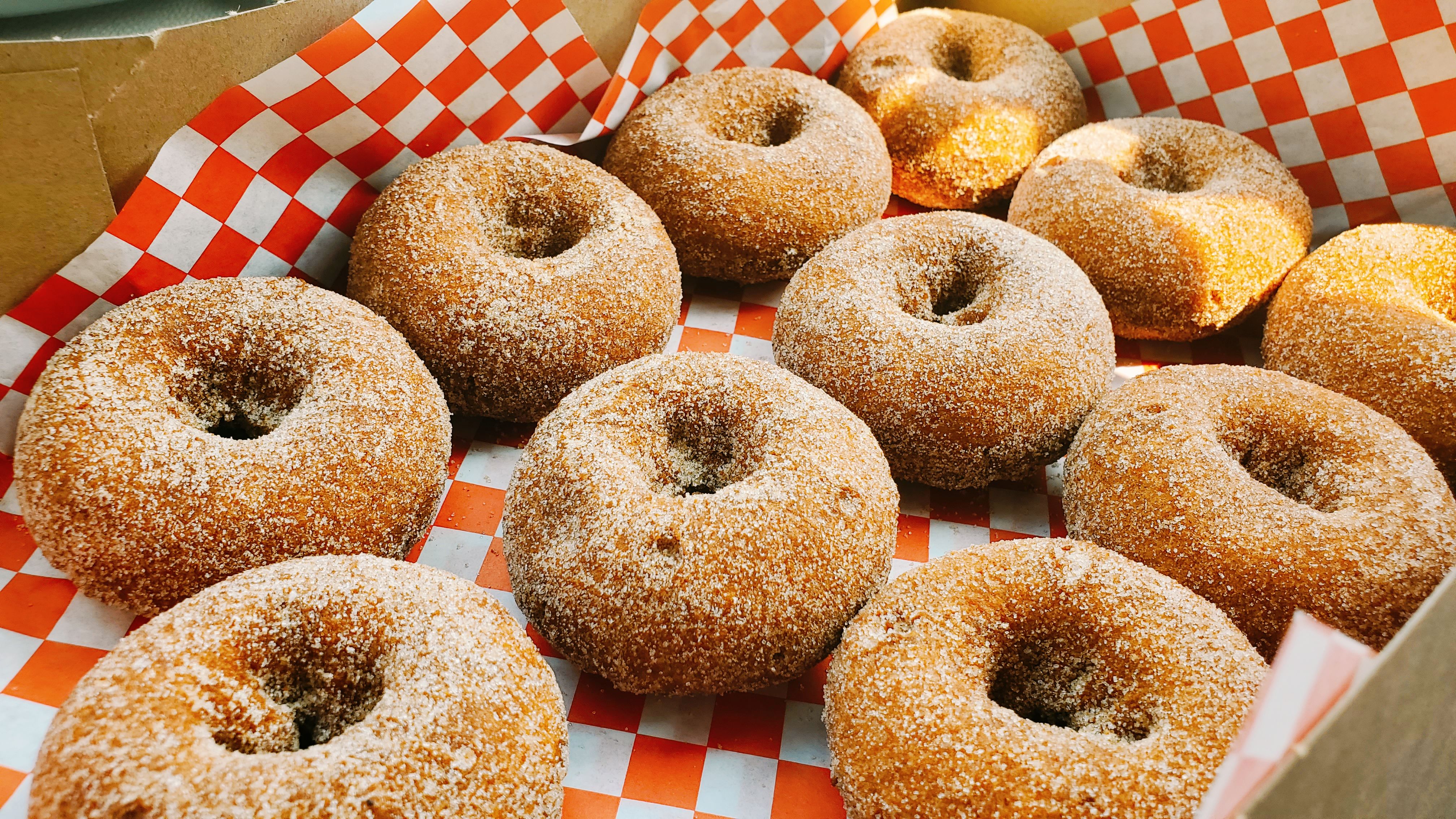 cider doughnuts with sugar coating sitting on checkered paper in a carbboard box