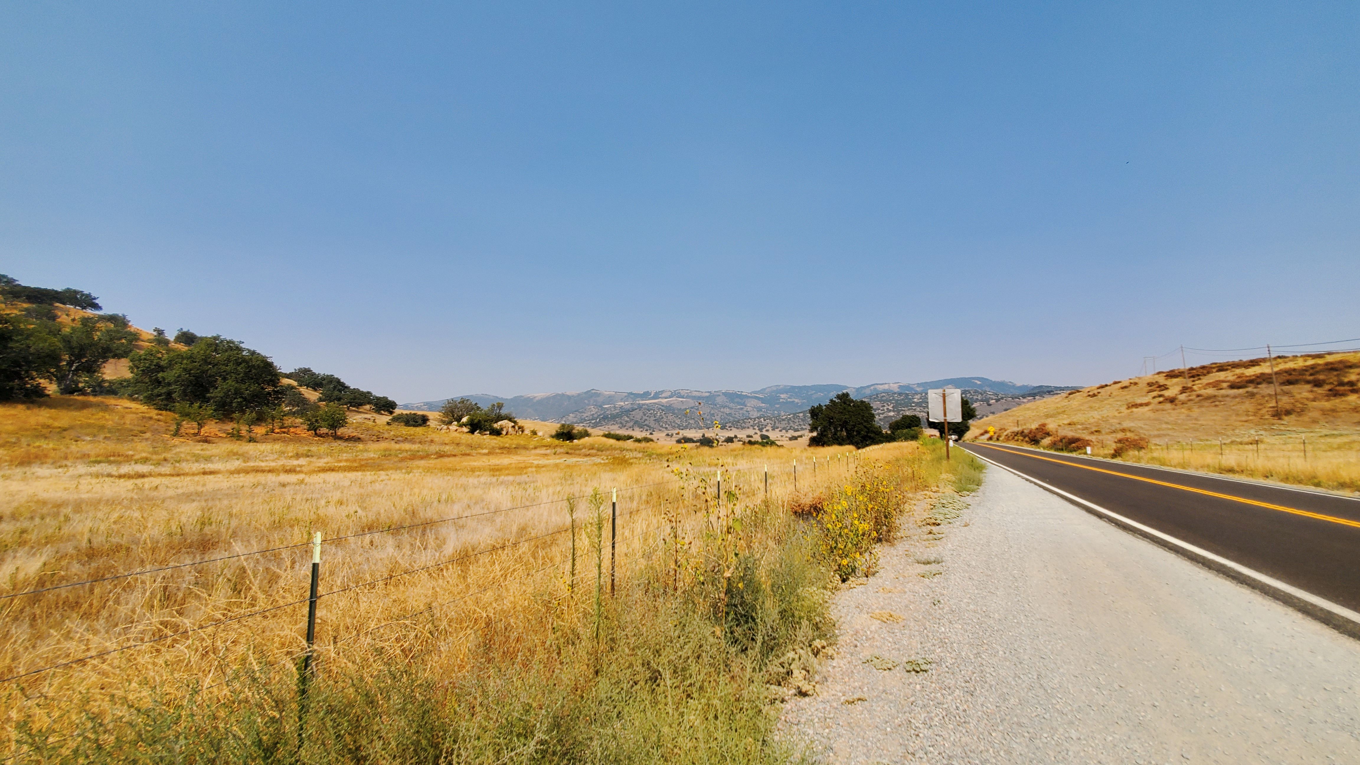 side of highway with golden brown fields and hazy mountains in the distance